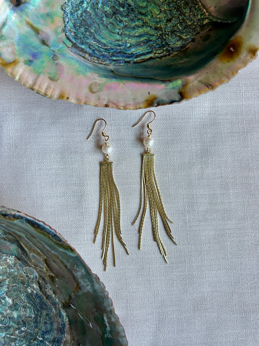 Gold tassel earrings with pearls on a shell background