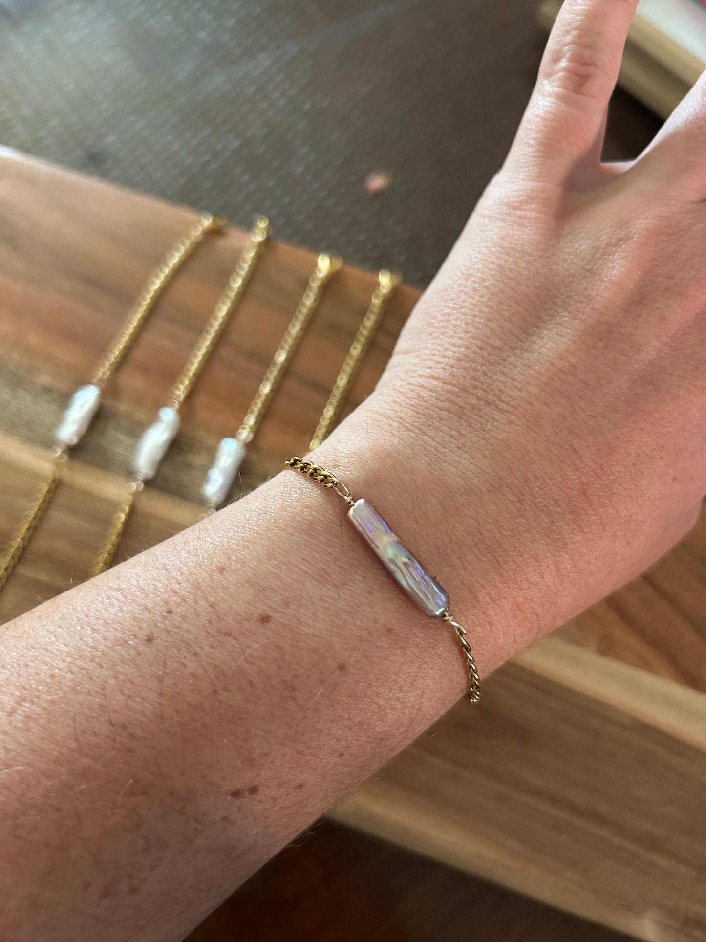A person wearing a pink elongated pearl gold bracelet 