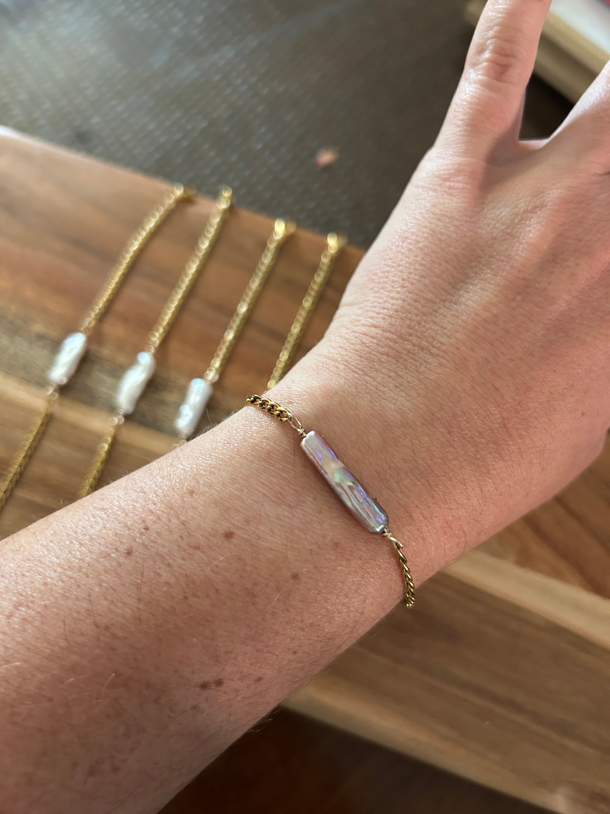 A person wearing a pink elongated pearl gold bracelet 